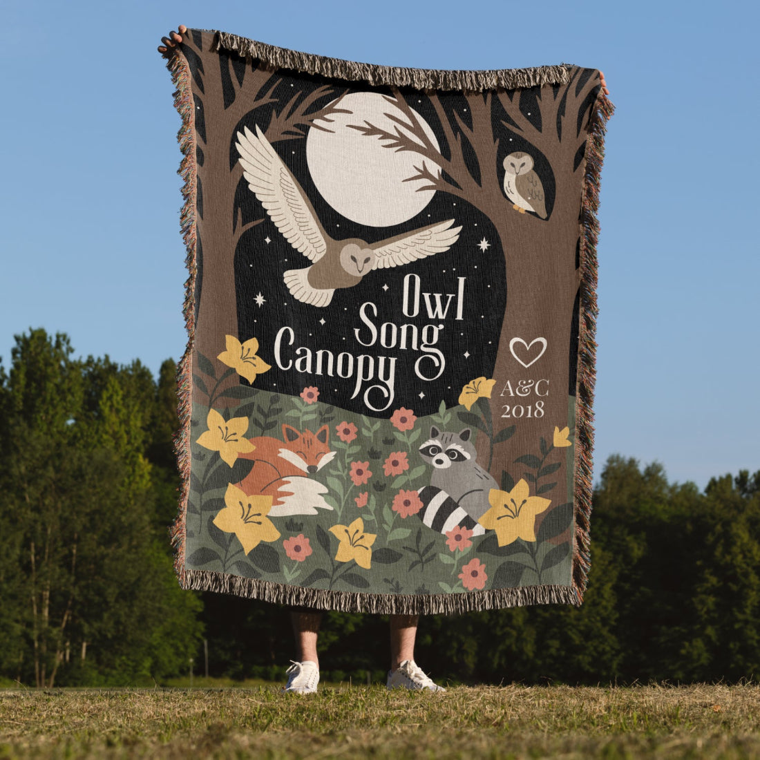 Person holding a 'Owl Song Canopy' blanket with nature-themed design outdoors.