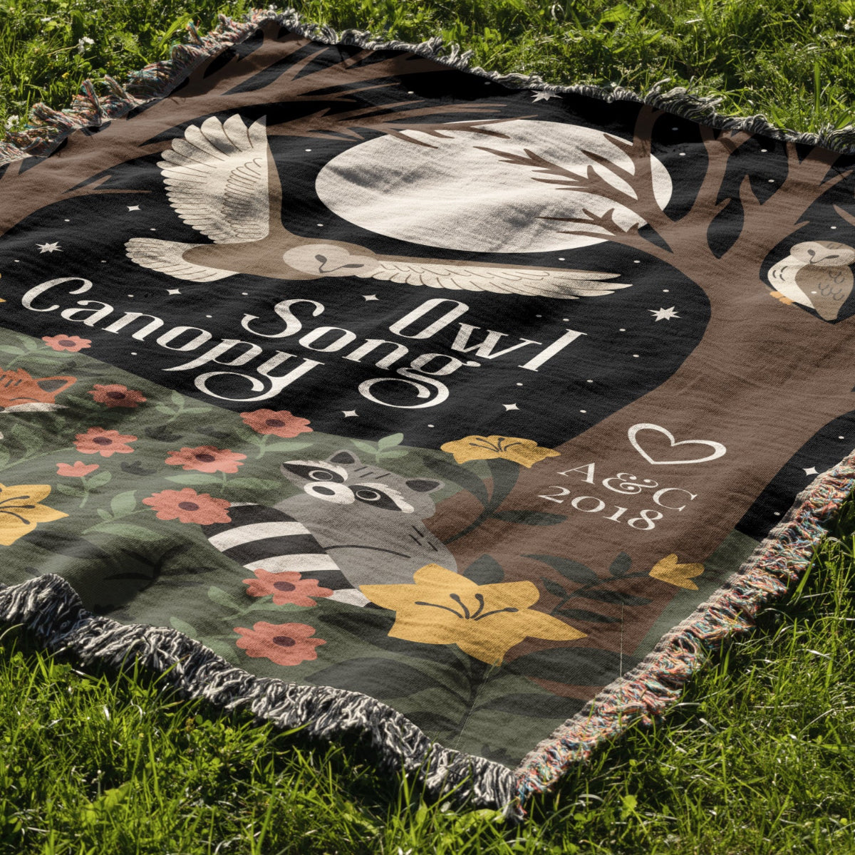 Blanket with 'Owl Song Canopy' design featuring an owl, raccoon, and flowers on grass.