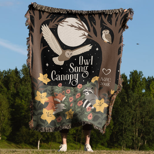 Person holding a decorative blanket with owl and nature design against a forest background