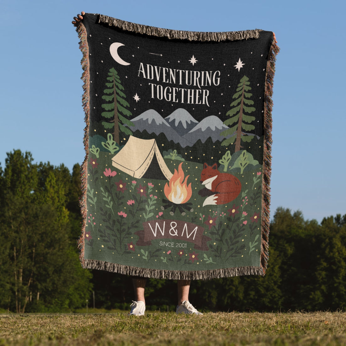 Blanket with camping design and text 'Adventuring Together' held by a person outdoors.