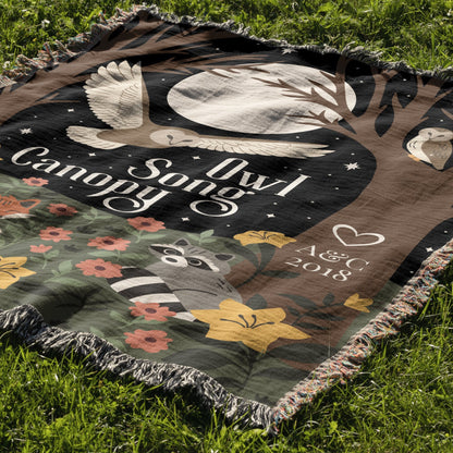 Blanket with 'Owl Song Canopy' design featuring an owl, raccoon, and flowers on grass.